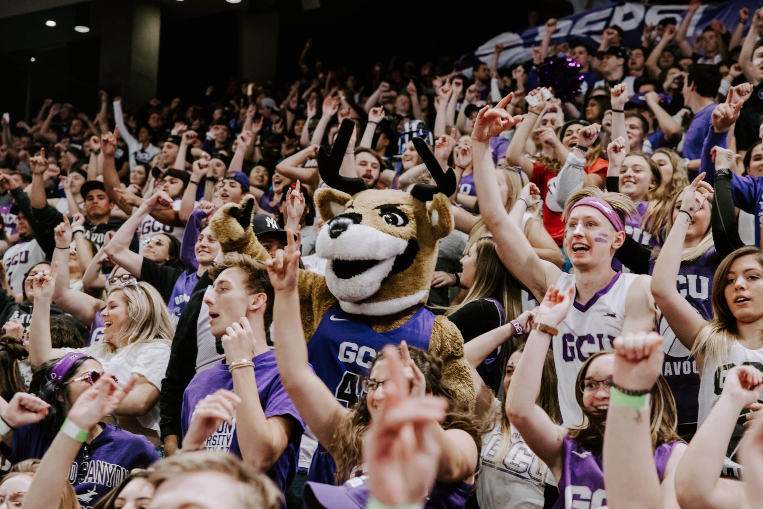 GCU Havocs student section, a sea of purple and white, dancing and cheering around their mascot.
