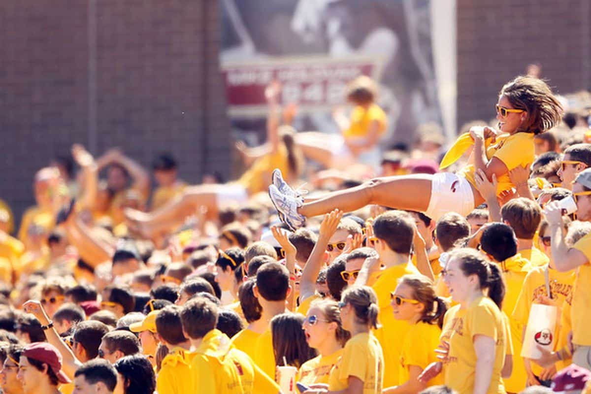 Boston College student section, united in yellow attire, with a woman crowd surfing, embodying the lively and spirited atmosphere of the event