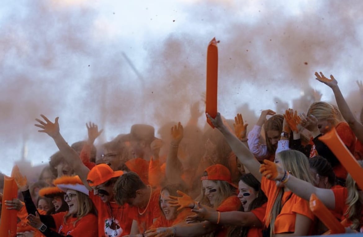 Student section dressed in orange rallies during the football game and engages the crowd with an orange powder toss.