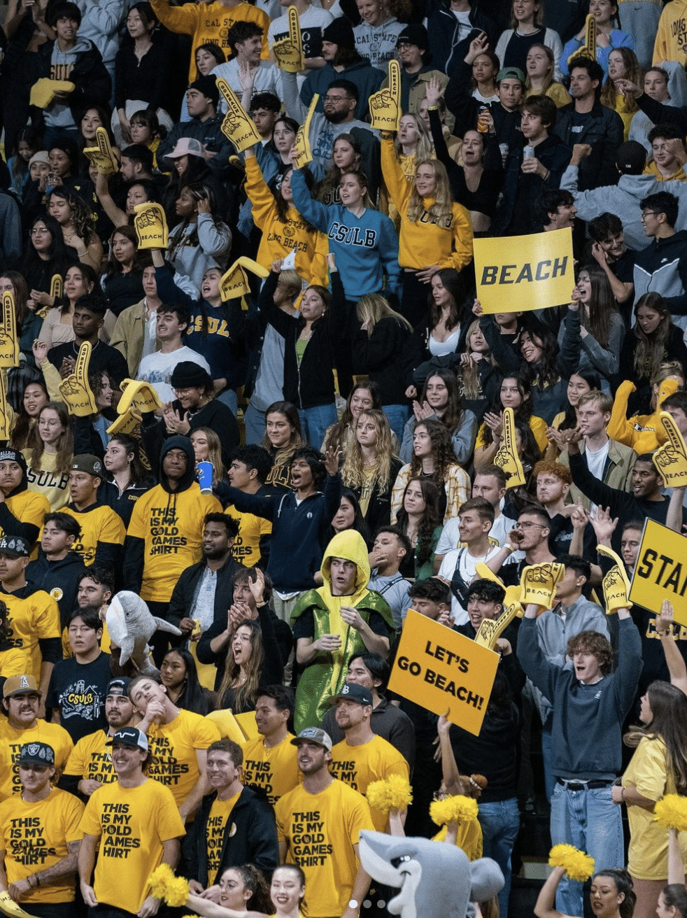 LSBU Sandpit student section, dressed in yellow, passionately cheering at a men's basketball game with energetic enthusiasm, rallying with 'Let's Go Beach' spirit.