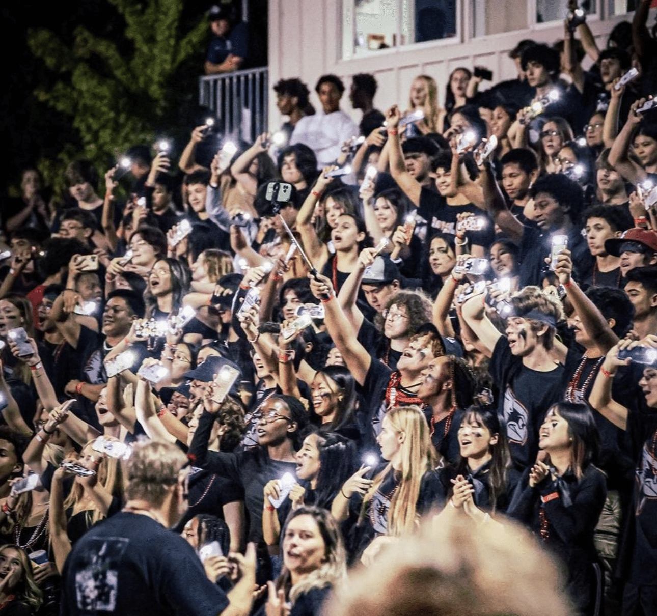 Laguna Beach High School student section in the bleachers, waving their phone lights, illuminating the stands with a sea of lights and school spirit.