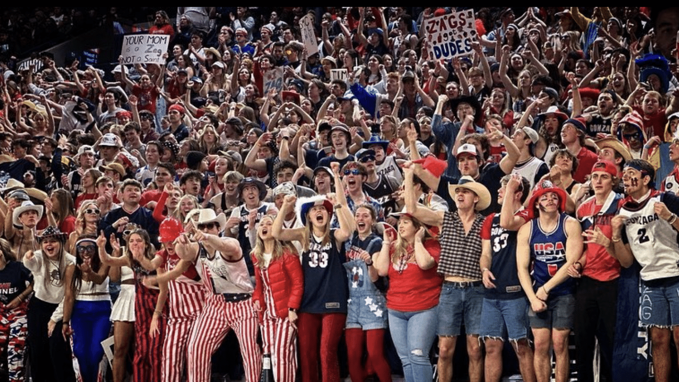 Gonzaga Kennel Club student section, dressed in navy and red, fervently cheering at a basketball game, showcasing their team loyalty and spirit.