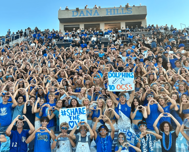 the student section of Dana Hills High School holds their hands up in the shape of a heart to pose for the camera.