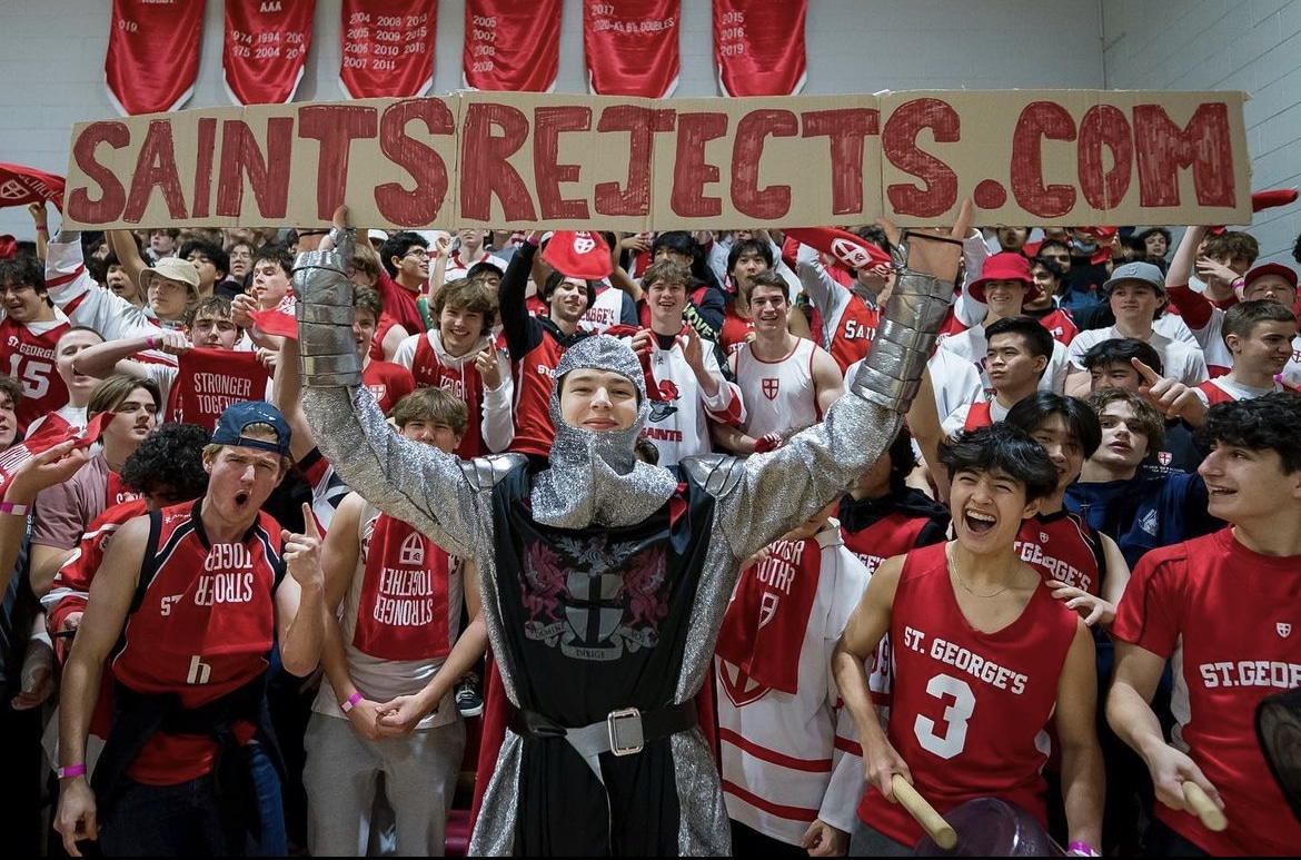 St. George's student section joyfully cheering while holding up a sign that reads 'saintsrejects.com,' displaying their school spirit and enthusiasm.
